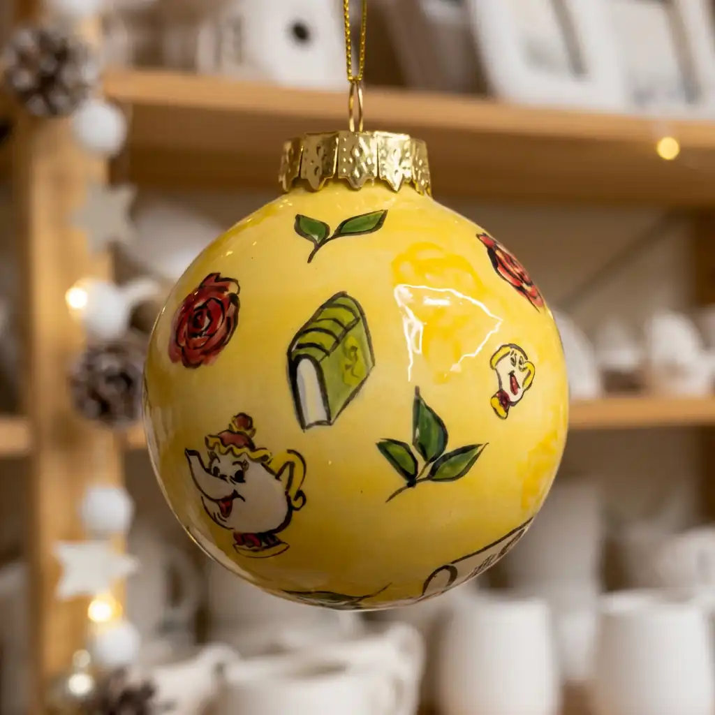 Yellow ceramic Christmas bauble painted with roses, leaves, a book and a teapot
